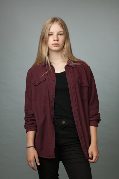 工作室肖像的一个金发少女在酒红色衬衫和黑色牛仔裤在灰色的背景图片下载