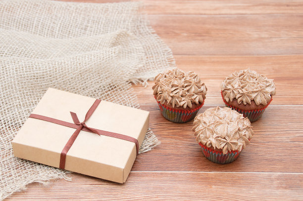一盒礼物和三个纸杯蛋糕。布朗木制背景。图片下载