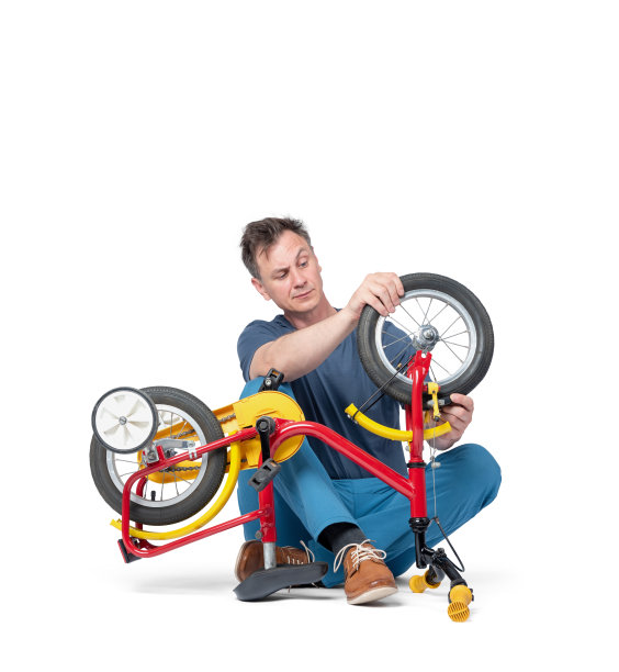 一个穿着便服的男人正在修理一辆儿童自行车，手里拿着一个轮子，孤立地站在白色的背景上。图片下载