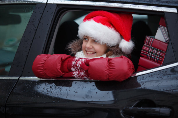 女孩戴着圣诞老人的帽子坐在汽车后座上，看着外面图片下载