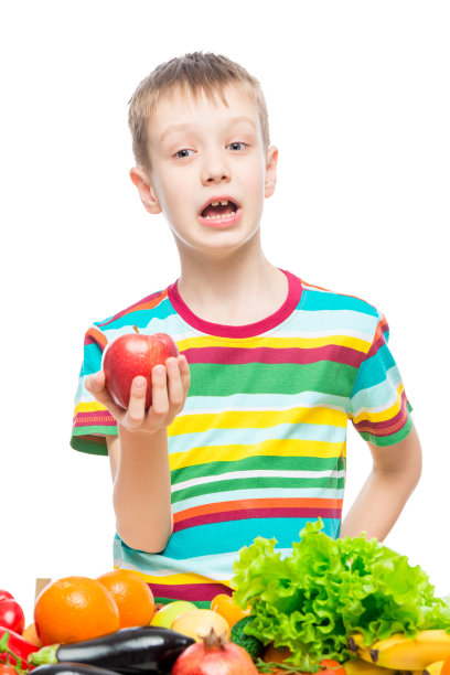 一个男孩的垂直肖像与一个红熟的苹果在工作室在白色的背景孤立图片下载