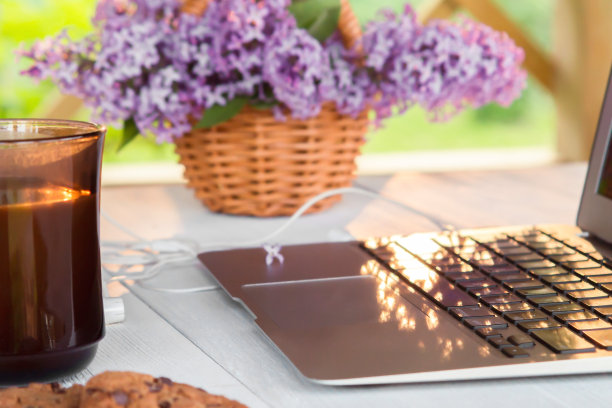 夏日阳台上的白色木桌上放着笔记本电脑、一杯咖啡、饼干和一篮丁香花——这是远程工作、在线商务和自主创业的概念图片下载