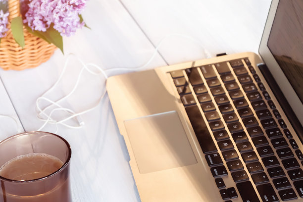 夏日阳台上的白色木桌上放着笔记本电脑、一杯咖啡、饼干和一篮丁香花——这是远程工作、在线商务和自主创业的概念图片下载