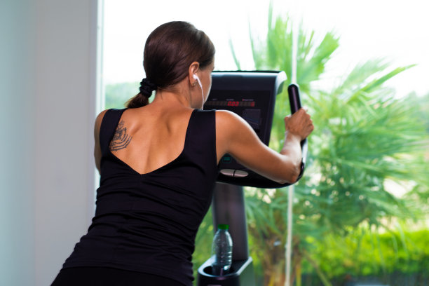 在减肥女性健身馆锻炼自行车有氧运动。女性用耳机听音乐。运动员、建设者、肌肉、生活方式图片下载