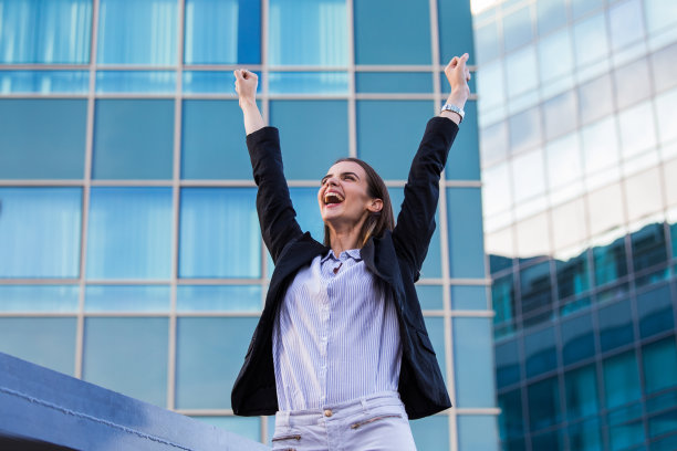 在背景的摩天大楼里，身着西装的女商人在完成交易后欣喜若狂。理念:商业、技术、经济、工作和成功图片下载
