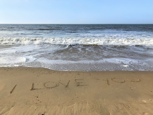 在阳光明媚的海滩上写下我爱你的话，用棍子写在沙子上，由海浪，概念社交媒体照片在柔软的金色沙滩上书写字母，多塞特，英国海边海岸线的景色图片下载