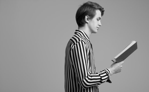 年轻英俊的男子在条纹衬衫读一本书在灰色的背景图片下载