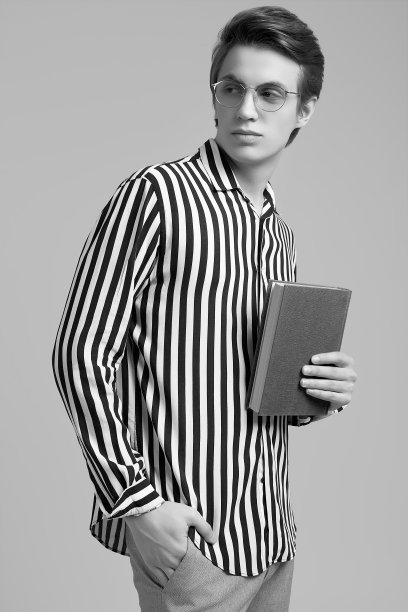 年轻男子在条纹衬衫摆姿势与一本书在灰色背景图片下载