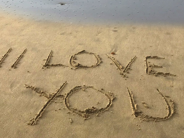 在阳光明媚的海滩上写下我爱你的话，用棍子写在沙子上，由海浪，概念社交媒体照片在柔软的金色沙滩上书写字母，多塞特，英国海边海岸线的景色图片下载