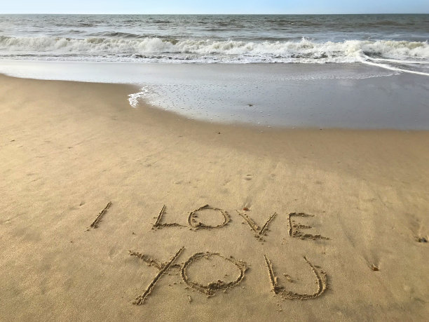 在阳光明媚的海滩上写下我爱你的话，用棍子写在沙子上，由海浪，概念社交媒体照片在柔软的金色沙滩上书写字母，多塞特，英国海边海岸线的景色图片下载