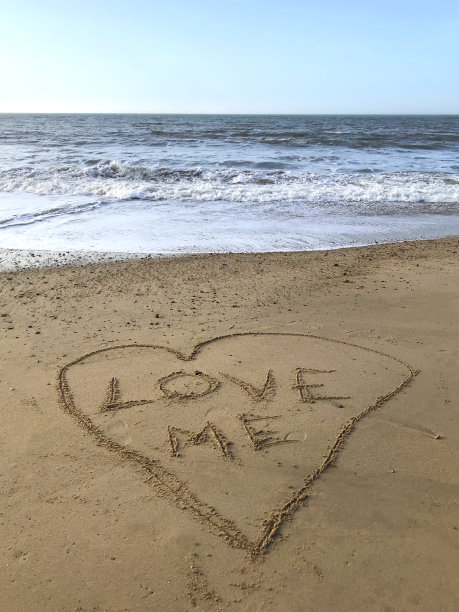 在阳光明媚的海滩上写下爱我的话写在里面，用棍子在沙子上画心，由海浪，概念社交媒体照片在柔软的金色沙滩上书写字母，多塞特，英国海边海岸线的景色图片下载