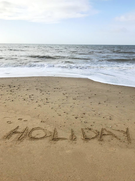 这是一张在阳光明媚的海滩上书写的照片，用棍子在沙子上写下节日的单词，由海浪，概念社交媒体上的照片，这是在英国多塞特郡伯恩茅斯海滩柔软的金色沙滩上书写字母的照片图片下载