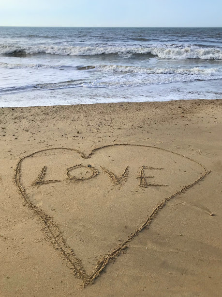 在阳光明媚的海滩上写着写在里面的爱的字在沙子上画着心，用棍子，海浪，概念社交媒体照片在柔软的金色沙滩上书写字母，多塞特，英国海边的海岸线图片下载