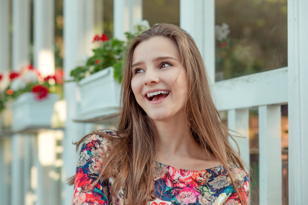 快乐优雅的年轻女子在时髦的夏季花卉连衣裙摆姿势与红色的木白色篱笆。图片下载