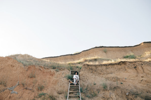 创意照片的年轻时尚的女人放松在热带岛屿海滩。时髦的波西米亚女孩戴着帽子坐在海边沙滩上的木楼梯上。暑假。空间的文本图片下载