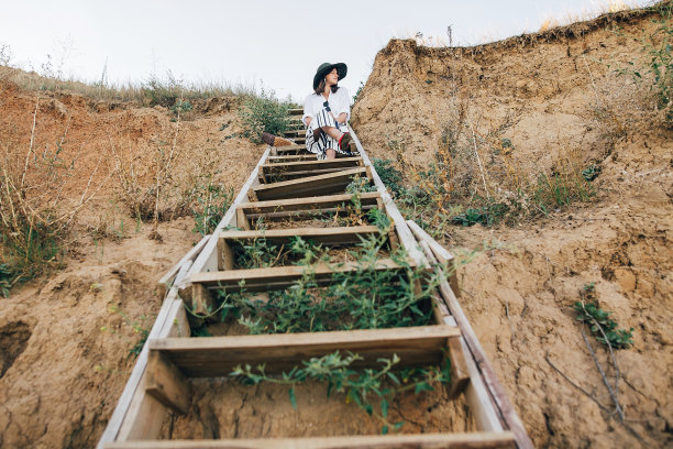 创意照片的年轻时尚的女人放松在热带岛屿海滩。时髦的波西米亚女孩戴着帽子坐在海边沙滩上的木楼梯上。暑假。空间的文本图片下载