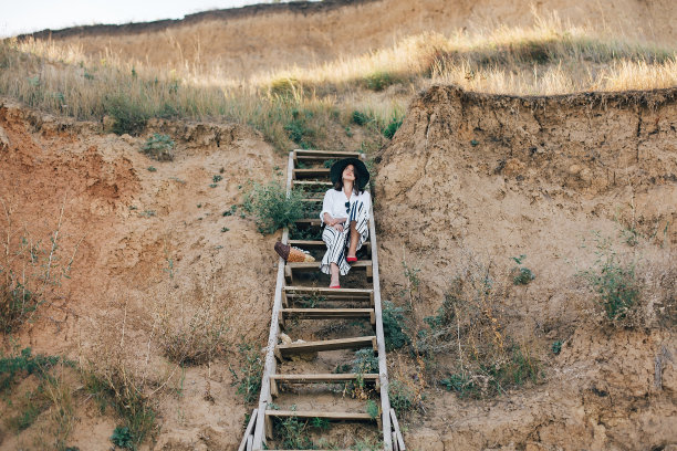 创意照片的年轻时尚的女人放松在热带岛屿海滩。时髦的波西米亚女孩戴着帽子坐在海边沙滩上的木楼梯上。暑假。空间的文本图片下载
