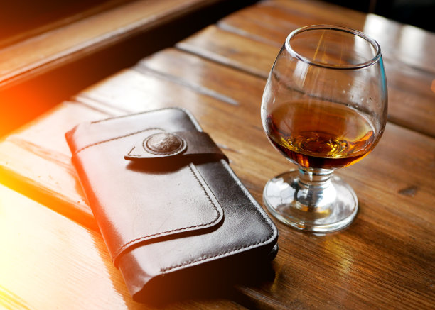 一杯威士忌或其他强烈的琥珀色酒精饮料和皮革棕色钱包上的黑色反射台面工作室背景，水平图片图片下载