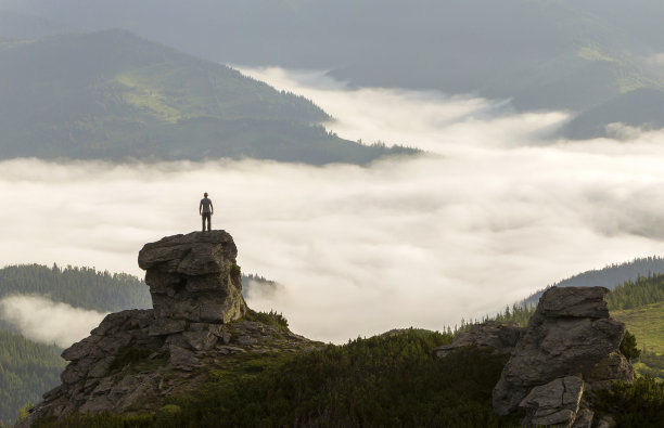 运动员攀岩游客的剪影在高岩石形成的山谷充满白色的蓬松的云和雾，覆盖常绿的森林山坡在晴朗的天空背景下。图片下载