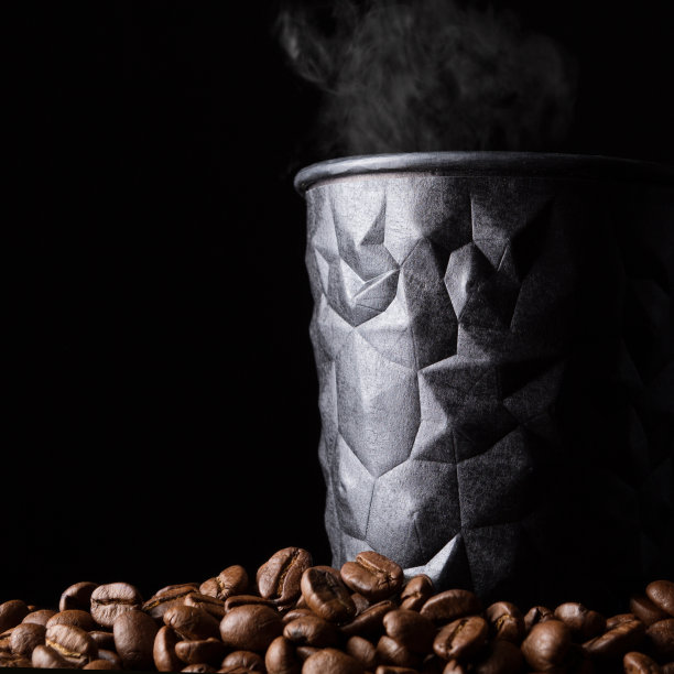黑色硬纸板咖啡杯放在一堆咖啡豆上，玻璃上面有蒸汽，这是一种咖啡饮料的概念，在黑色的背景上图片下载