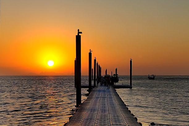 日出时，人们沿着码头走到海滩。工人们乘船航行。图片下载