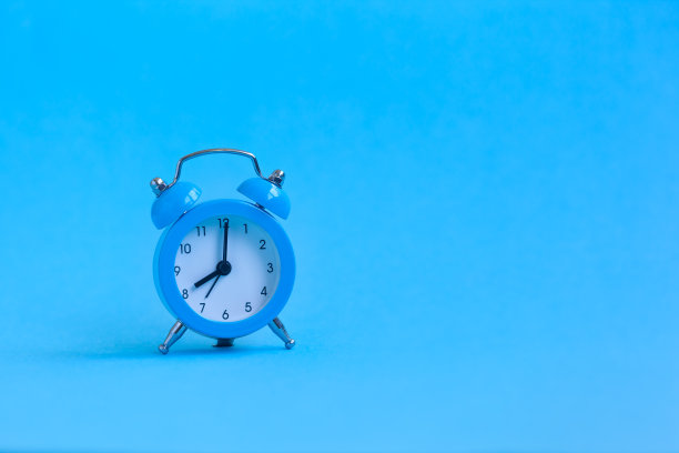蓝色背景上的蓝色闹钟。极简主义。图片下载