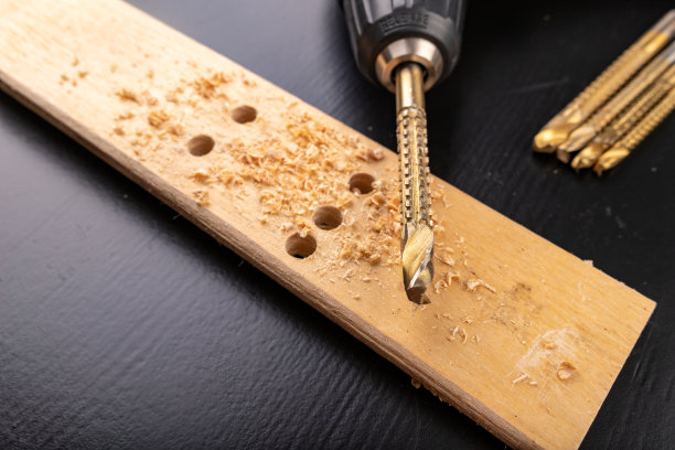 在一块刨过的干木头上钻孔。用螺丝刀在车间打洞。黑暗的背景。图片下载