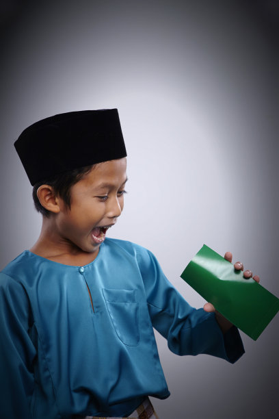 淘气的马来男孩拿着绿色的信封支票数目的钱在里面图片下载