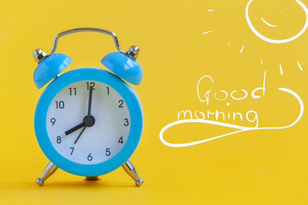 蓝色闹钟在黄色背景与文字早上好。极简主义。对比的概念。图片下载