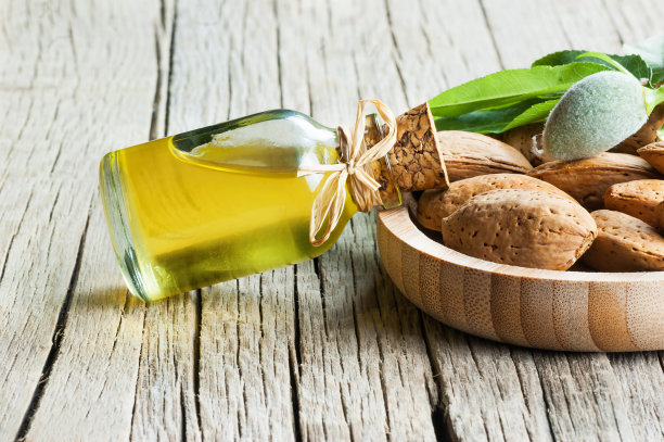 玻璃瓶杏仁油和杏仁坚果，杏仁壳竹碗在木背景与绿色新鲜的生杏仁在杏仁树枝图片下载