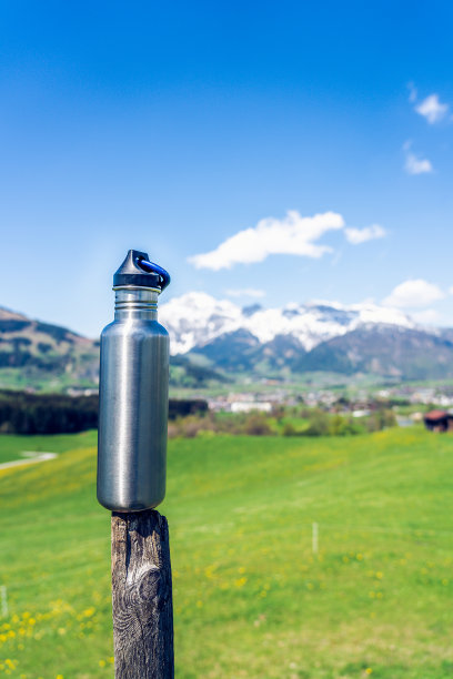 金属水瓶放在木柱上。背景是山脉和绿色植物。图片下载