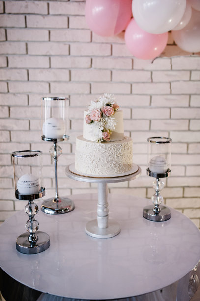 桌子上有婚礼蛋糕，蜡烛和鲜花。照片墙，婚礼装饰空间或地方从白色和粉色气球和白色砖墙。图片下载