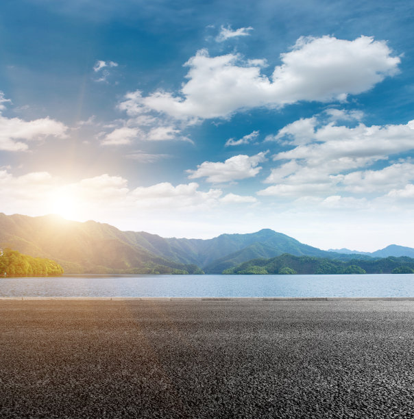 在一个阳光明媚的秋日，在蓝天白云的映衬下，我们可以看到群山和宽阔的湖泊，柏油路在湖前图片下载