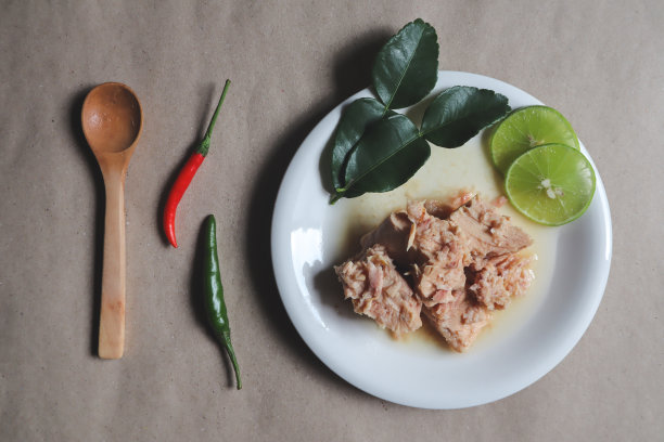 捣碎的金枪鱼片放在白色的盘子里，配上柠檬和辣椒，用木勺，放在即食垫上，食物图片下载