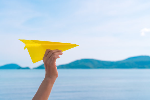 女人手握纸飞机在蓝天白云在热带日落海滩抽象的背景。复制空间旅行冒险和自由的概念。图片下载