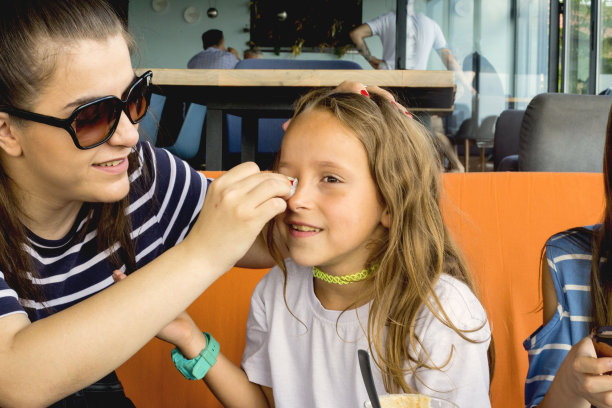 在夏日的咖啡馆里，美丽的长发妈妈用湿纸巾擦着女儿的脸。抗菌餐巾纸和新鲜概念图片下载