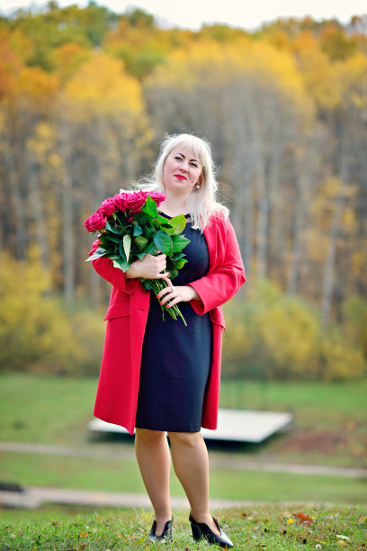 美丽的女人，金发碧眼，身穿红色外套，在公园里捧着一束红玫瑰。阳光明媚的一天。女性尺码加xxl。关闭了。俯视图图片下载