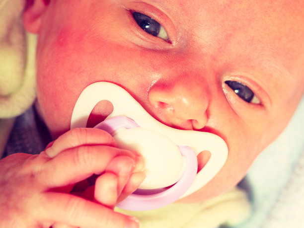一个小新生儿躺着，嘴里叼着奶头的特写图片下载