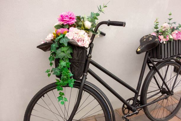复古自行车作为花坛装饰的外部元素。一辆黑色的老自行车靠墙站着，车上有两个花篮，里面放着漂亮的花。艺术装饰特写微距图片下载