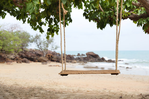 老绳木秋千在大自然的绿树，沙滩和蓝天的背景图片下载