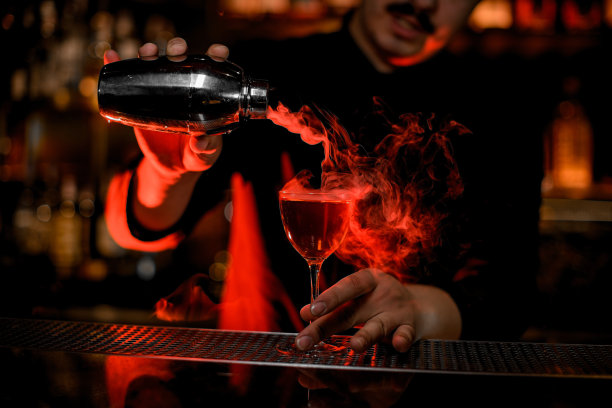 职业男调酒师从钢质摇酒器中向鸡尾酒杯中注入烟雾图片下载