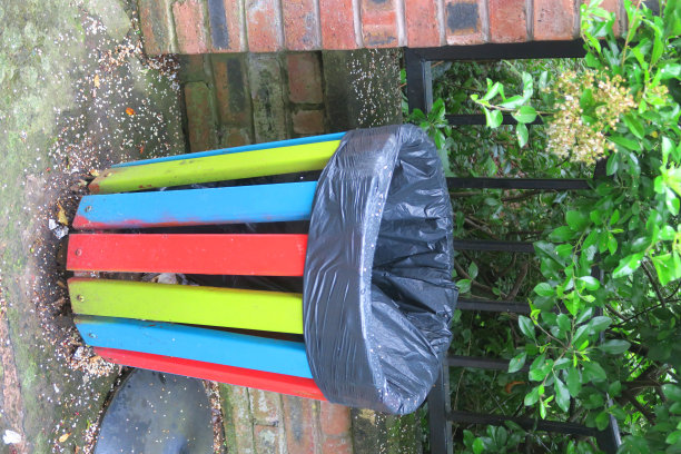 街道、公园、花园、停车场旁的彩虹色垃圾桶/装有黑色塑胶垃圾袋的垃圾桶图像，以控制污染和乱扔垃圾。图片下载