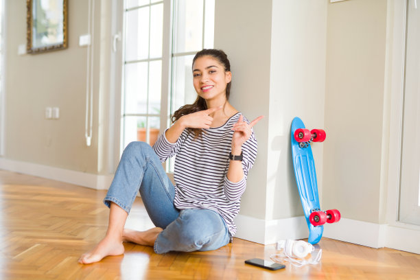 年轻女人坐在地板上玩滑板图片下载