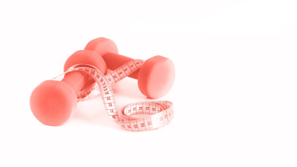 健康的概念。时髦的珊瑚色背景下的哑铃和卷尺。Copyspace图片下载