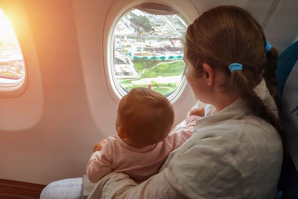 妈妈带着小孩望着窗外的飞机向地面降落。带一岁以下的女婴旅行图片下载