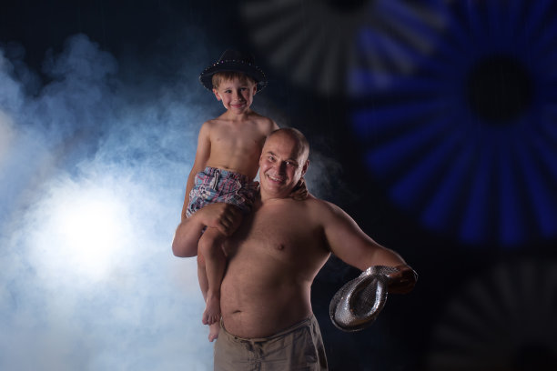 马戏团演员和一个孩子在舞台上。爸爸和儿子一起表演。在舞台灯光中，一个男人扶着一个小男孩的肩膀图片下载