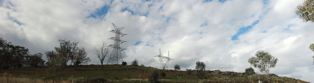 在一个多云的日子里，俯瞰高耸的高能量电力架空输电塔，俯瞰澳大利亚本土的树木和植物，澳大利亚乡村图片下载