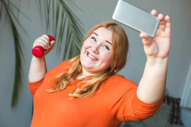 胖乎乎的女人在运动家中站着开心地拿着哑铃自拍图片下载