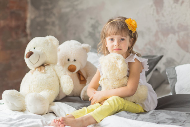 一个小女孩坐在床上玩泰迪熊的肖像图片下载