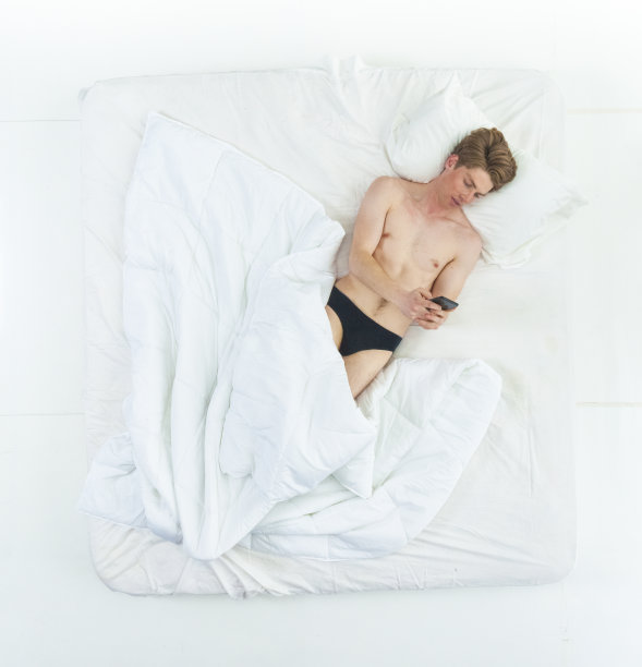 英俊的男人躺在床上，赤膊上阵，还在打电话图片下载